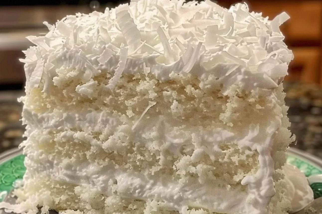 Slice of creamy coconut cake with coconut flakes and frosting on a plate